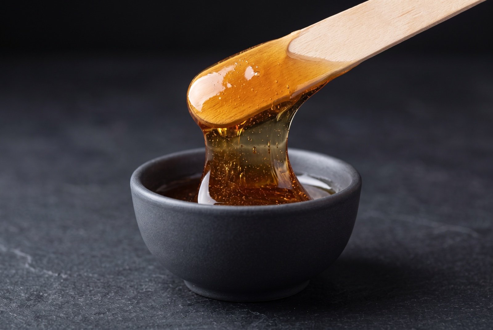 Amber sugaring paste lifted on a wooden spatula